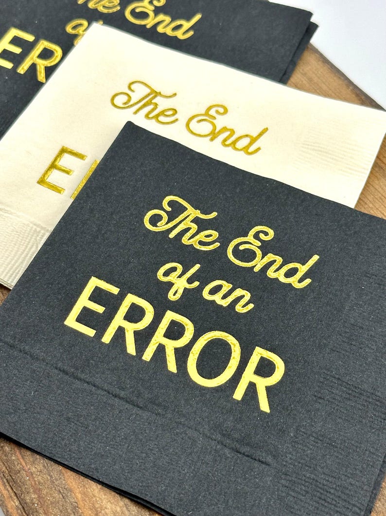 Three square paper napkins, two black and one cream, with "The End of an ERROR" in gold foil script on each.