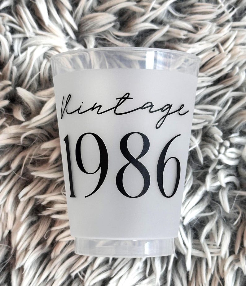 A single frosted plastic cup with "vintage" in black script and "1986" in black block letters is shown on a fuzzy gray background.