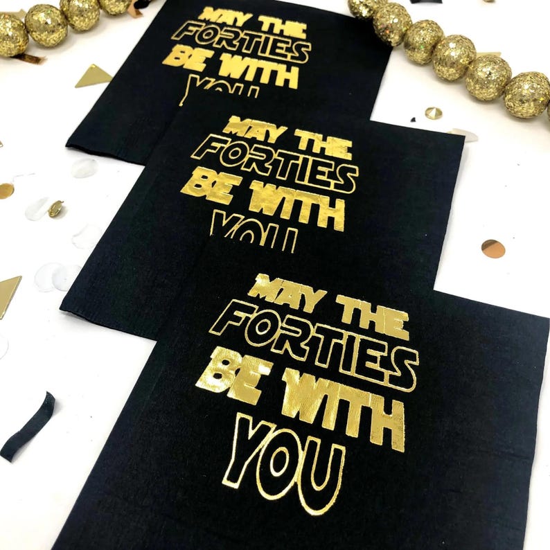 Three black paper napkins featuring gold text that reads May the Forties be with you, surrounded by gold beads and confetti.