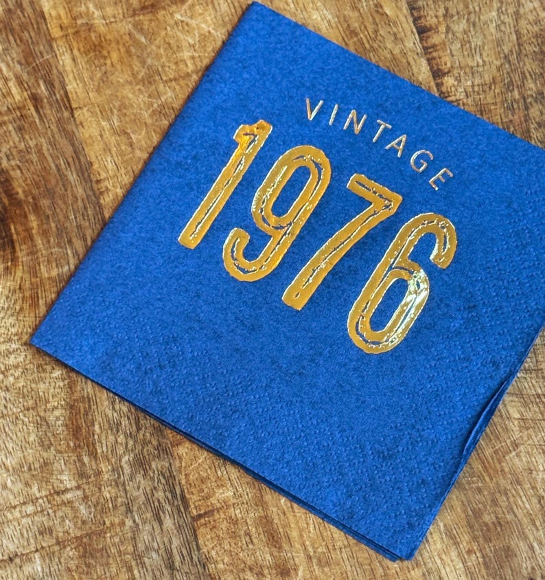 May include: A blue felt square with the word "VINTAGE" above the gold metallic numbers "1976". The item is on a wooden surface.