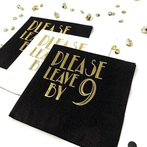 Stacked paper napkins in black and white featuring gold foil stamped text that reads Please Leave By 9, scattered with gold confetti on a white surface.