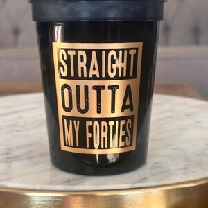 Front view of a black reusable cup printed with the gold phrase Straight Outta My Forties.