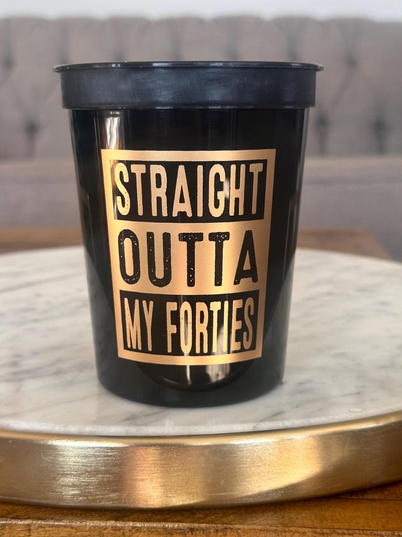 Front view of a black reusable cup printed with the gold phrase Straight Outta My Forties.