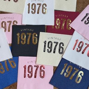 May include: A collection of square paper napkins in various colors, each printed with the word "VINTAGE" above the number "1976". The numbers are in gold, red, and black, with a variety of background colors.