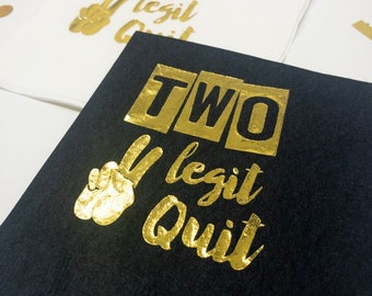 May include: Black paper napkin with gold foil lettering that reads "TWO legit quit" and a peace sign.