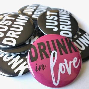 May include: A stack of black and white button pins with the text "Just Drunk" and a single pink button pin with the text "Drunk in Love" in white.