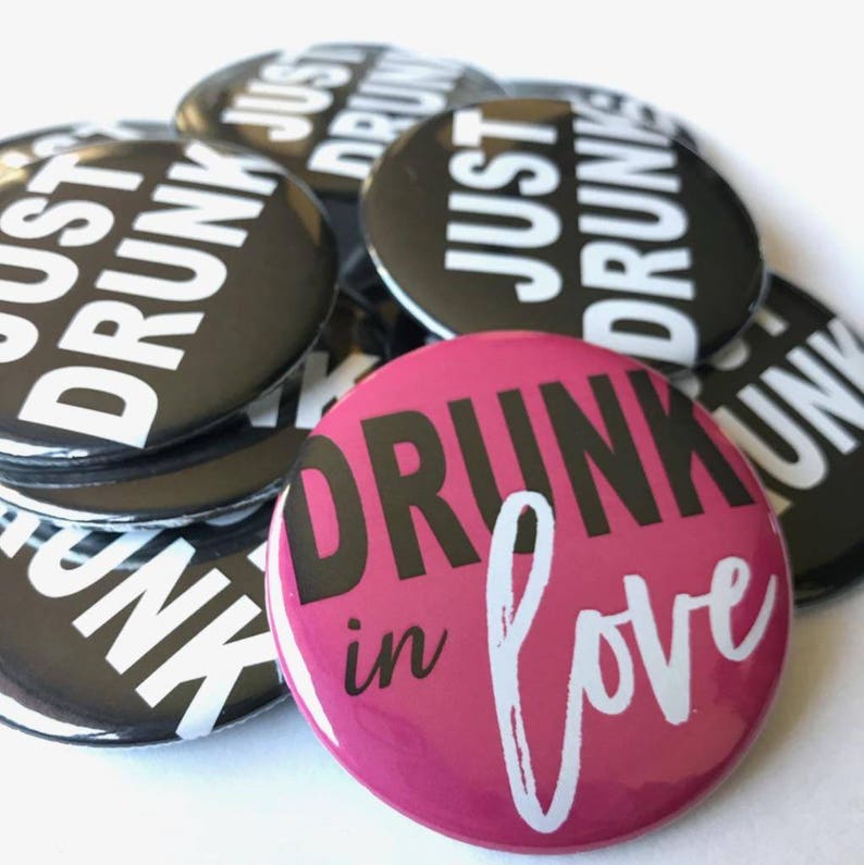 May include: A stack of black and white button pins with the text "Just Drunk" and a single pink button pin with the text "Drunk in Love" in white.