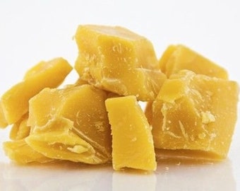 May include: A pile of golden yellow beeswax chunks. The pieces vary in size and shape, with a rough, textured surface. The wax appears solid and opaque, with a natural, organic appearance.
