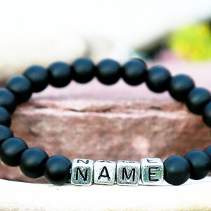 Puede incluir: Pulsera de cuentas negras con cuentas de letras plateadas que deletrean la palabra "NAME".