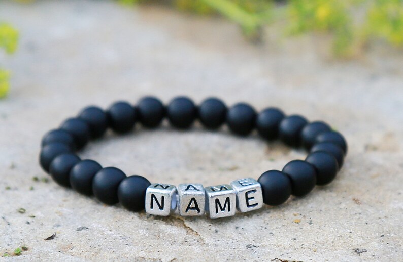 Puede incluir: Pulsera de cuentas negras con cuentas de letras plateadas que deletrean la palabra "NAME".