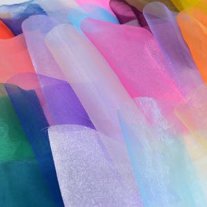 May include: A collection of colorful sheer fabric rolls in various shades of pink, blue, purple, green, and orange. The fabric is translucent and has a slight shimmer.