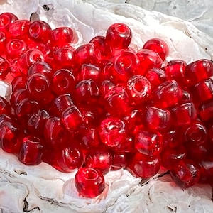May include: A large pile of red glass beads. The beads are round and have a smooth, shiny finish.