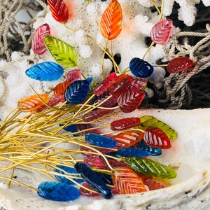 May include: A bunch of colorful glass leaf-shaped beads on gold wire stems. The beads are arranged in a shell.