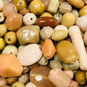 May include: A collection of natural stone beads in various shapes and sizes, including oval, round, and rectangular. The beads are in shades of brown, beige, and cream.