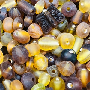 May include: A collection of amber glass beads in various shapes and sizes. The beads are a mix of brown, yellow, and clear glass, with some having a frosted finish.