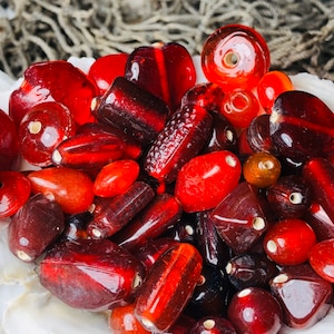 May include: A collection of red glass beads in various shapes and sizes. The beads are translucent and have a glossy finish.