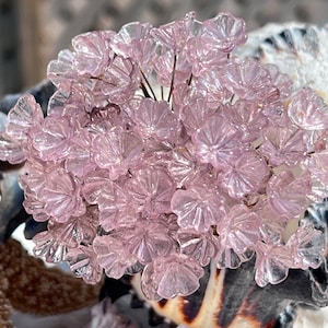 以下が含まれることがあります： 繊細で半透明なピンク色のガラスの花の集まり。花は花束にアレンジされており、繊細で虹色の輝きを放っています。