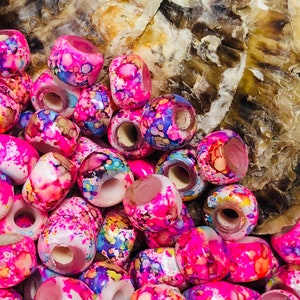 May include: A close-up of a pile of colorful, pink, white, and blue wooden beads. The beads have a marbled, swirled pattern and are perfect for jewelry making.