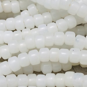 May include: Close-up of strands of white, barrel-shaped beads. The beads are strung together, creating a textured surface. The beads are opaque and have a smooth, matte finish. Ideal for jewelry making.