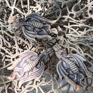 May include: Three ceramic dragon figurines with wings outstretched. The dragons are painted in shades of brown, white, and blue, with a skeletal design.