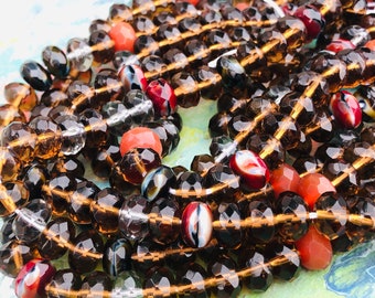 May include: A strand of brown faceted glass beads with a mix of clear and opaque beads. There are also a few red and white beads with a swirl pattern.