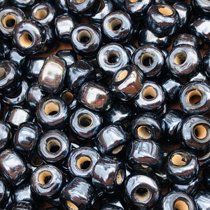May include: A close-up of a pile of black wooden beads with a shiny, glossy finish. The beads have a large hole in the center.
