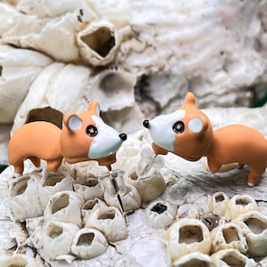May include: A pair of orange and white dog-shaped stud earrings. The earrings are made of polymer clay and have a cute, cartoonish style.