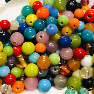May include: A collection of colorful glass beads in various sizes and shades, including red, orange, yellow, green, blue, and purple. The beads are round with a hole through the center, suitable for jewelry making or crafts.