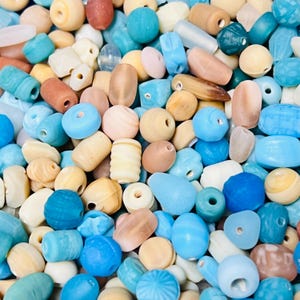 May include: A collection of colorful glass beads in shades of blue, brown, and white. The beads are various shapes and sizes, including round, oval, and teardrop.