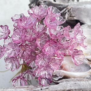 以下が含まれることがあります： 繊細なピンク色のガラスの花の集まりで、複雑な花びらのディテールが特徴です。 花は細い茶色の茎に配置され、花の配置を形成しています。 半透明の花びらは光を捉えています。