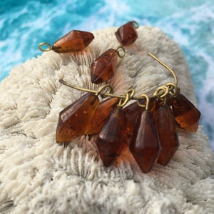 May include: A set of amber glass teardrop beads with gold-toned metal loops. The beads are strung on a wire and are ready to be used in jewelry making.