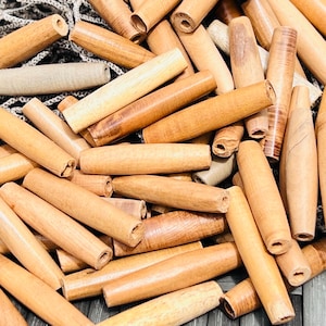 May include: A large pile of natural wood dowels, all the same size and shape, with a light brown color. The dowels are arranged in a random pattern, with some overlapping.