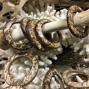 May include: A group of brown coconut shell rings with a natural wood grain pattern. The rings are stacked on top of each other and are surrounded by white coral.