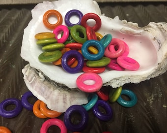May include: A collection of colorful wooden rings in a white seashell. The rings are various shades of pink, red, orange, yellow, green, blue, and purple.