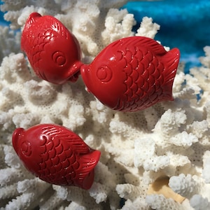 May include: Four red fish figurines with detailed scales and a textured surface. The figurines are arranged on a white coral background.