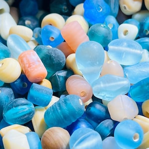 May include: A collection of colorful glass beads in shades of blue, white, and pink. The beads are various shapes and sizes, including round, oval, and teardrop.