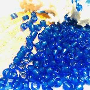 May include: A large pile of bright blue glass beads, scattered on a white surface. The beads are round and have a shiny finish.