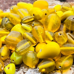May include: A collection of yellow glass beads in various shapes and sizes. The beads are translucent and have a glossy finish.