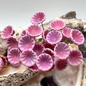 May include: A cluster of pink ceramic flower beads with a ridged petal design. The beads are arranged on thin, gold-colored wires, creating a floral arrangement. The flowers are a soft pink color with a hint of purple in the center.