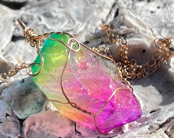 May include: A rainbow iridescent crystal pendant wrapped in gold wire, hanging from a gold chain necklace. The pendant is a natural, rough-cut crystal with a variety of colors, including green, yellow, orange, pink, and purple.