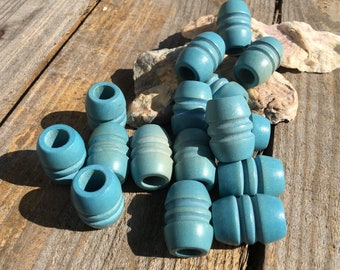 Puede incluir: Un grupo de 15 cuentas de madera azul turquesa con un diseño acanalado. Las cuentas están dispuestas en una pila sobre una superficie de madera.