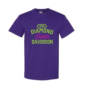 May include: A purple t-shirt with the text "Diamond Diva's Davidson" in green and pink. The design includes a diamond graphic above the text. The shirt has short sleeves and a crew neck.