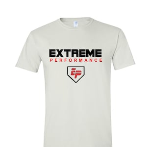 May include: Cream-colored t-shirt with the words "EXTREME PERFORMANCE" in black and red lettering. Below the text is a black and red logo. The shirt is a short-sleeved crew neck.