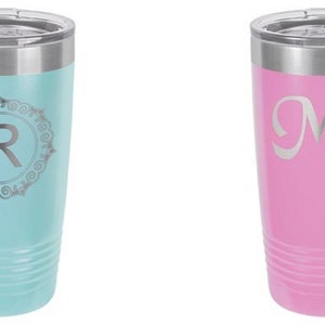 May include: Two insulated tumblers. One is light blue with a silver lid and a decorative silver letter "R" inside a circular design. The other is pink with a silver lid and the silver letter "M" with the name "Maria".