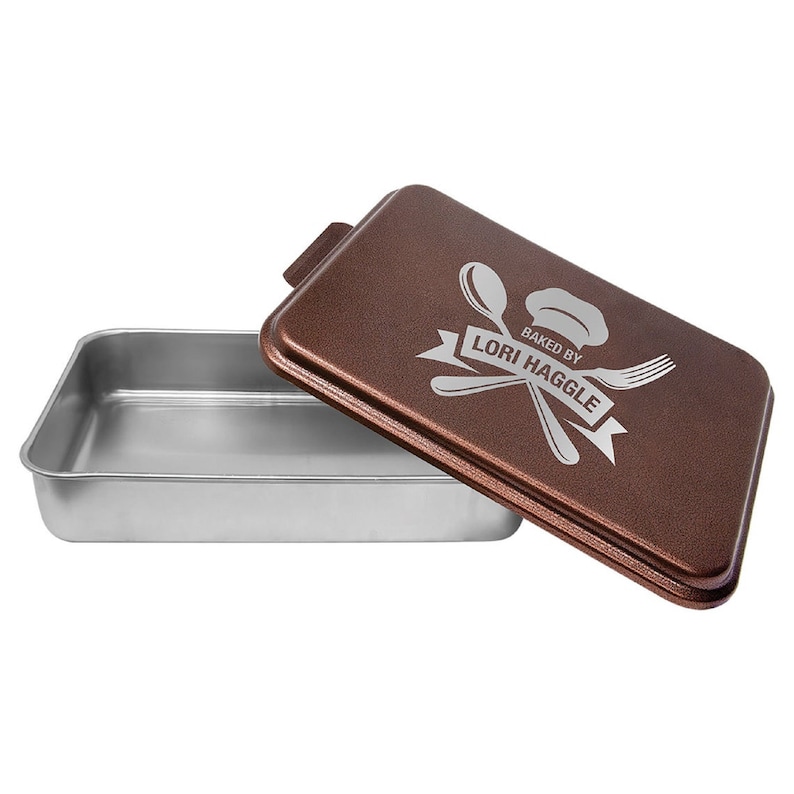 May include: A copper-colored baking pan with a lid. The lid has a silver inscription that reads "Baked by Lori Haggle" with a chef's hat, crossed utensils, and a banner.