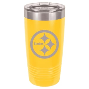 May include: Yellow insulated tumbler with a silver lid. The tumbler features the Pittsburgh Steelers logo in gray, with the word "Steelers" above the team's logo. The tumbler is cylindrical with a ridged design near the bottom.