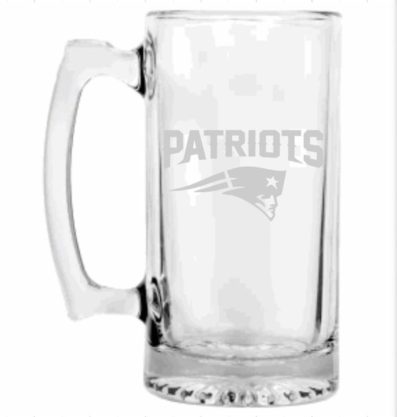 May include: Clear glass beer mug with a rectangular shape and a large handle. The word "PATRIOTS" is etched on the front, along with the team's logo. The mug is designed for holding beverages.