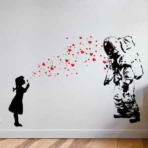 Può includere: Una silhouette in bianco e nero di una ragazza che soffia cuori rossi verso una silhouette in bianco e nero di un astronauta. L'astronauta indossa una tuta spaziale e un casco. I cuori sono sparsi nell'aria tra la ragazza e l'astronauta.