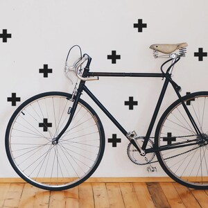 May include: A black bicycle with a white wall tyre and black plus signs on a white wall.