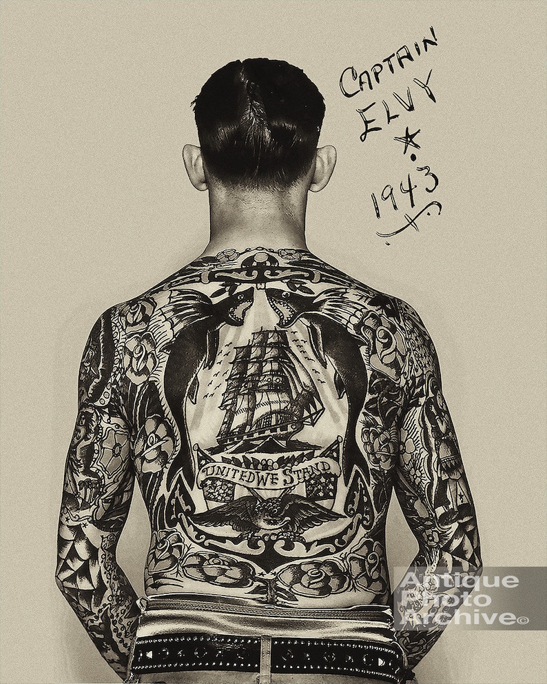 May include: A black and white photo of a man with a full back tattoo. The tattoo features a ship, an eagle, an anchor, and the words "United We Stand". The man's name, "Captain Elvy", and the year "1943" are written on the top right corner of the photo.